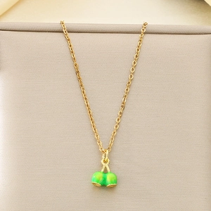 Detail of a gold-plated necklace featuring a vibrant green cherry pendant on a beige surface