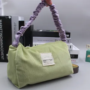 Detail of light green corduroy bag with purple ruffled handle and white text label