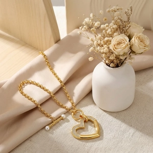 Détail du collier cœur doré avec strass et perle sur un tissu de fond beige