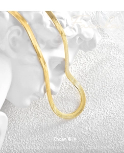 Detailed close-up of a polished gold flat snake chain choker on a white sculpture