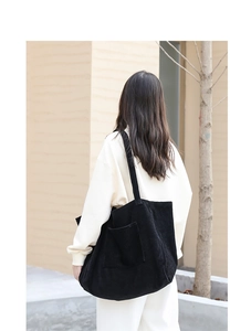 Model view of a large black corduroy shoulder bag showing capacity and draping effect