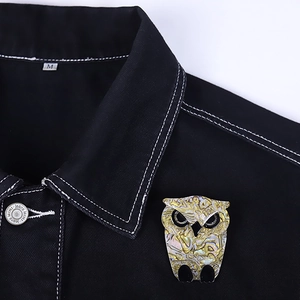 Colorful acrylic owl brooch with shell texture pinned on a black denim jacket collar