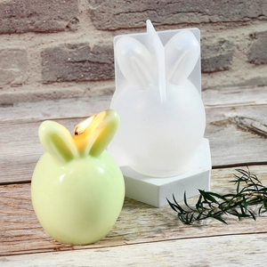 Detail of bunny silicone mold with a light green finished candle on wooden background