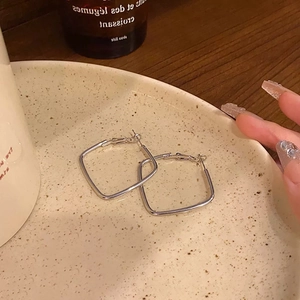 Detailed view of silver square geometric hoop earrings on a vintage ceramic plate
