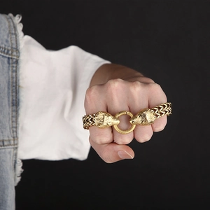 Detailed view of wolf heads on golden woven chain bracelet worn on a person's wrist