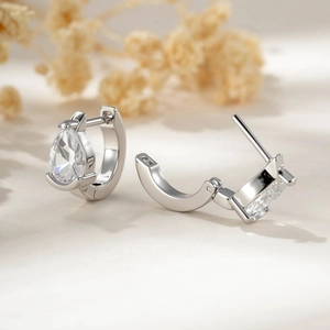 Silver hoop earrings with drop-shaped zircon crystals on a minimalist beige background