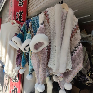 Detail of knit ponchos with faux fur collar and pom-poms featuring wavy weave patterns