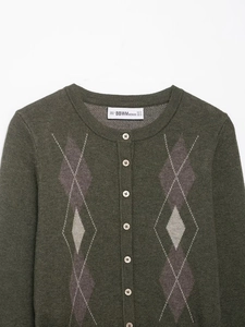Dettaglio del cardigan in maglia verde scuro con motivo a rombi, bottoni bianchi ed etichetta