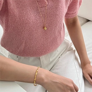 Detail of a minimalist gold braided chain bracelet on a model wearing pink knitwear