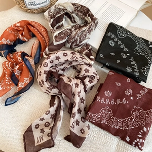 Flat lay of retro printed silk scarf necklaces in orange and coffee tones on white knit