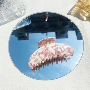 Close-up of pink acetate floral hair claw clip reflected on a mirror under blue sky