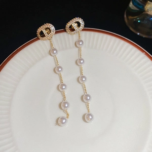 Detail of gold earrings with CD logo, sparkling crystals, and cascading white pearls