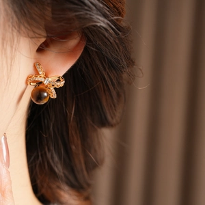 Close-up of golden bow earrings with zircon and tiger eye stones worn by a model