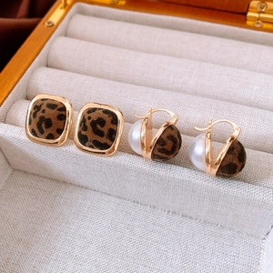 Macro shot of leopard print earrings and pearl studs in a beige velvet jewelry box