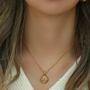 Close-up of golden necklace with a square pink gemstone and textured pendant base on a model