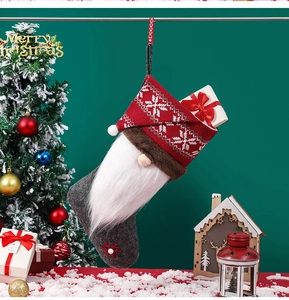 Detail of a red and grey knitted gnome Christmas stocking with festive decor accessories