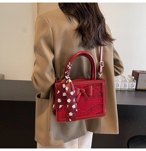 Detail of red bridal handbag featuring intricate lace embroidery and a stylish large bow