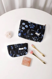 Close-up of two black linen cosmetic bags with blue floral embroidery on a white table