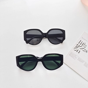 Flat lay of oversized black sunglasses with dark grey and green lenses on white surface