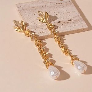 Detail of gold floral leaf earrings with tassels, sparkling rhinestones and white pearls
