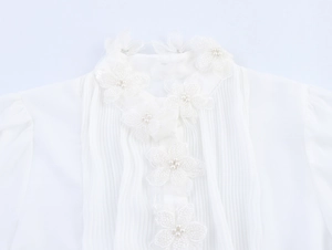 Detail der weißen Blusen-Halslinie mit zarten Spitzenblumen, Perlen und Plissee-Front