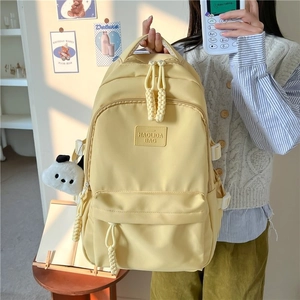 Detail of light yellow nylon backpack featuring side buckles and cute panda plush charm