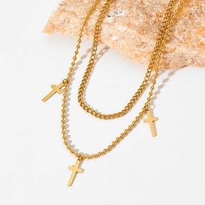 Detail of layered gold beaded and Cuban link chains with cross charms on a stone