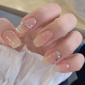 Pink gradient press-on nails with rhinestones on a hand against white lace sleeves