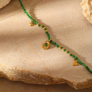 Detailed macro view of green natural stone beads and gold pendants on textured stone
