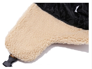 Dettaglio dei paraorecchie neri trapuntati con fodera in ecopelliccia beige e fibbia in plastica