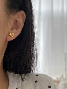 Close-up of elegant gold heart stud earring worn on ear with textured metal finish