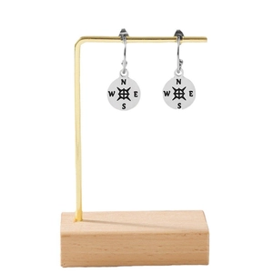 Minimalist compass hook earrings in polished stainless steel displayed on a wooden stand