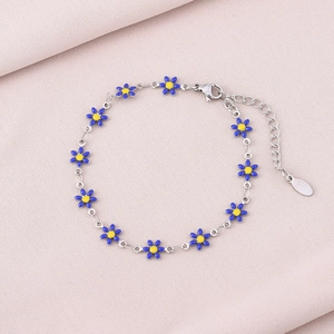 Macro view of silver daisy chain bracelet with blue enamel petals on pink fabric