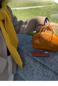 Close-up of a vintage leather Boston bag styled with a warm yellow knit scarf