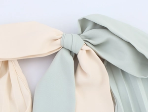 Detail showing a soft beige and mint green fabric bow with delicate texture on a pleated dress