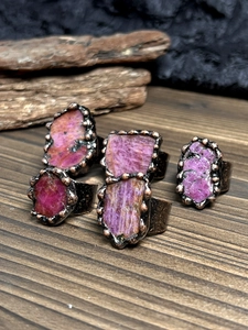 Detailed view of five raw pink ruby rings with textured bronze bands on wood