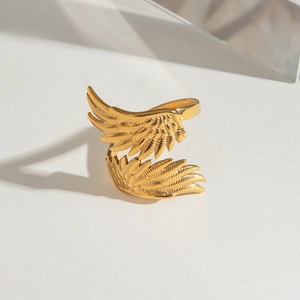 Golden stainless steel angel wing feather ring displayed on a modern glass background