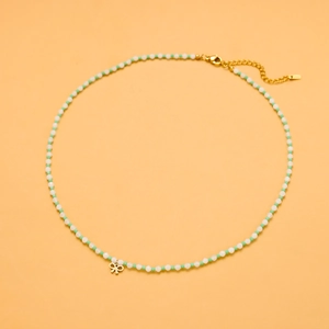 Detail of beaded necklace with white and green stones and a gold bow pendant
