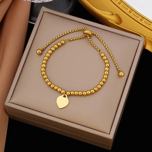 Adjustable gold stainless steel beaded bracelet with heart pendant on silk background
