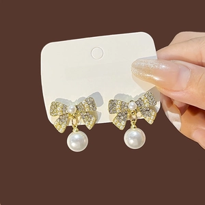 Detail of elegant gold butterfly earrings with sparkling crystals and a white pearl drop