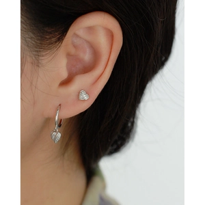 Close-up of a model wearing a small silver heart stud and heart charm hoop earring