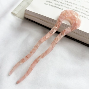 Macro view of a pink marble-textured acetate U-shaped hair pin on soft white fabric