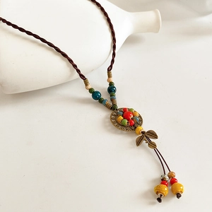 Detail of ethnic ceramic beaded necklace featuring a leaf pendant and bronze emblem