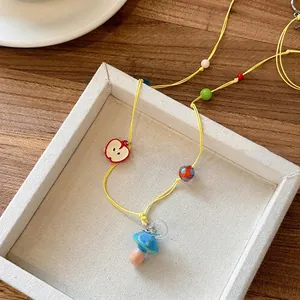 Detail of yellow wax rope necklace with apple and mushroom charms on a white tray