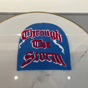 Detail of blue knit beanie featuring red and white Through The Storm jacquard lettering