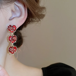 Detailed close-up of triple heart drop earrings with red enamel and gold rose relief