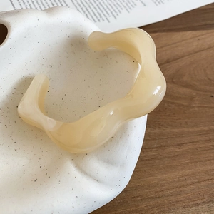 Close-up of a minimalist cream wavy acrylic open cuff bracelet on a ceramic tray