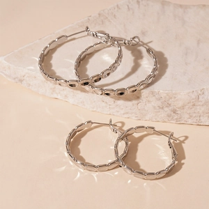 Macro view of silver geometric hoop earrings on a textured stone with water shadow effects