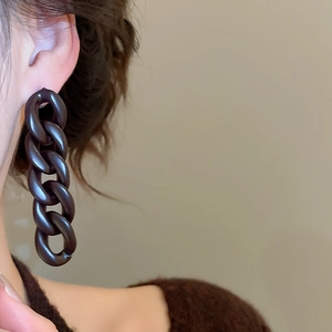 Detail of dark brown matte acrylic chain tassel earrings worn for a retro look