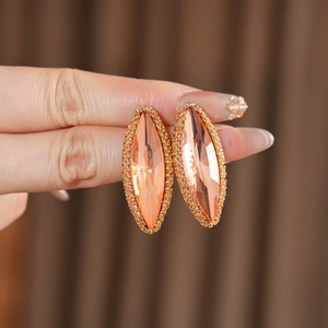 Macro shot of marquise-cut peach gemstone earrings with gold beaded edges in a retro style